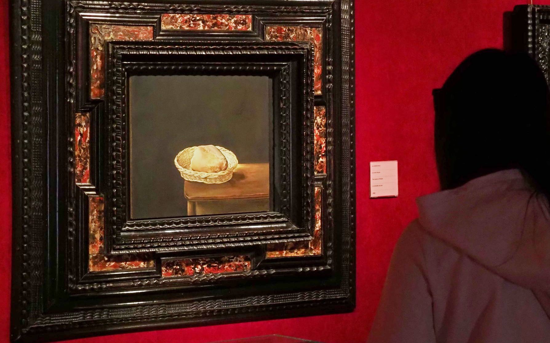 Basket of bread painting in ornate frame viewed by museum visitor.