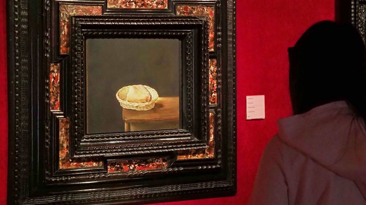 Basket of bread painting in ornate frame viewed by museum visitor.