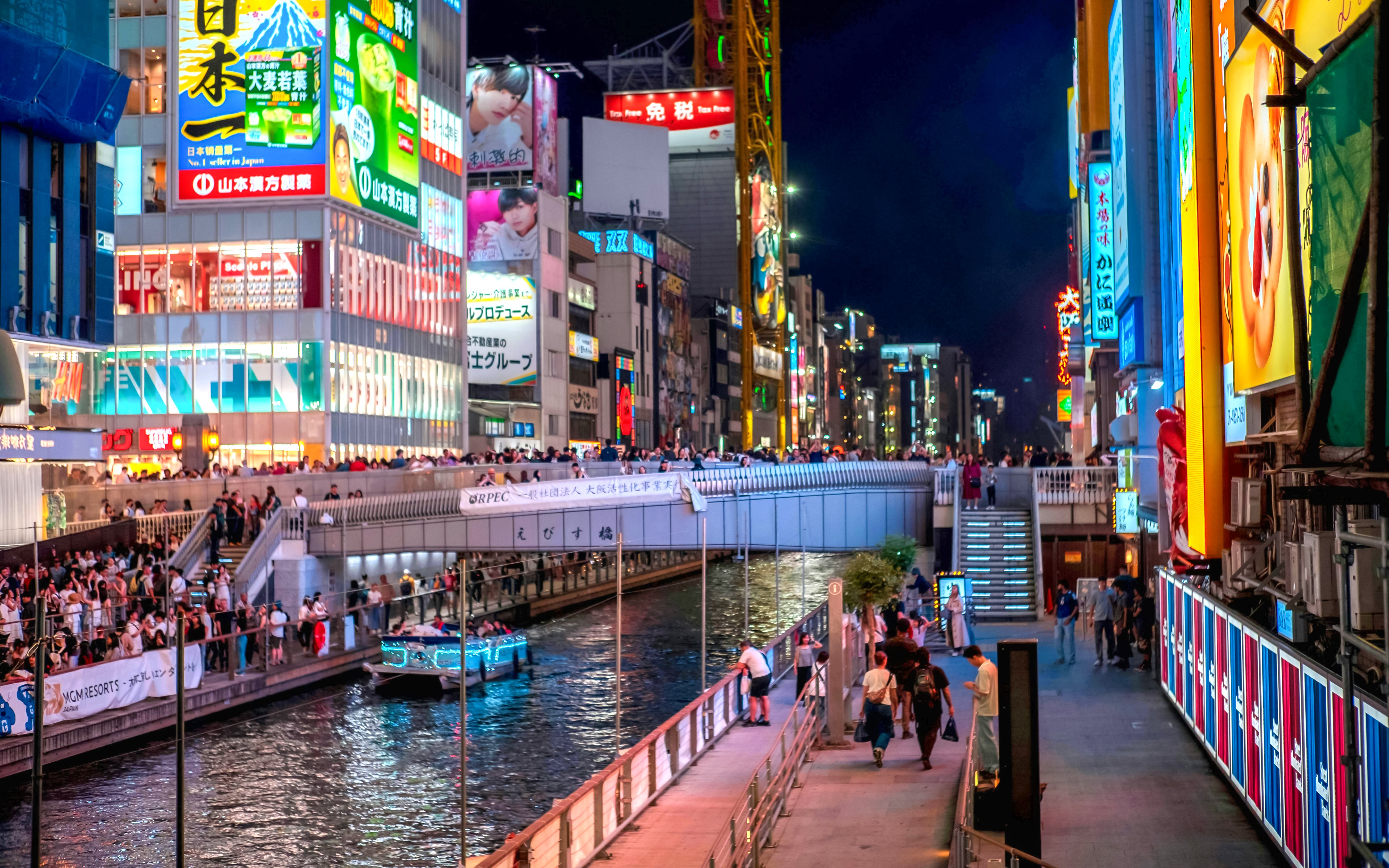 Ebisu Bridge over Dotonbori canal at night, Osaka, Japan, with illuminated signs and boat.