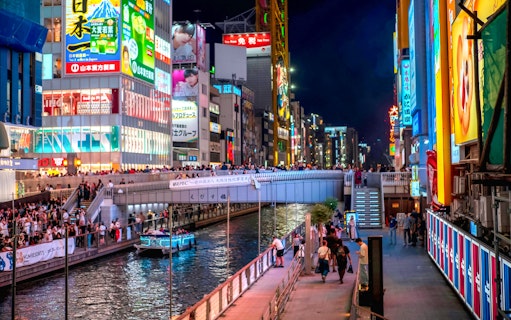 Ebisu Bridge over Dotonbori canal at night, Osaka, Japan, with illuminated signs and boat.