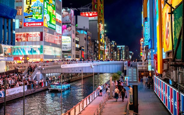 Ebisu Bridge over Dotonbori canal at night, Osaka, Japan, with illuminated signs and boat.