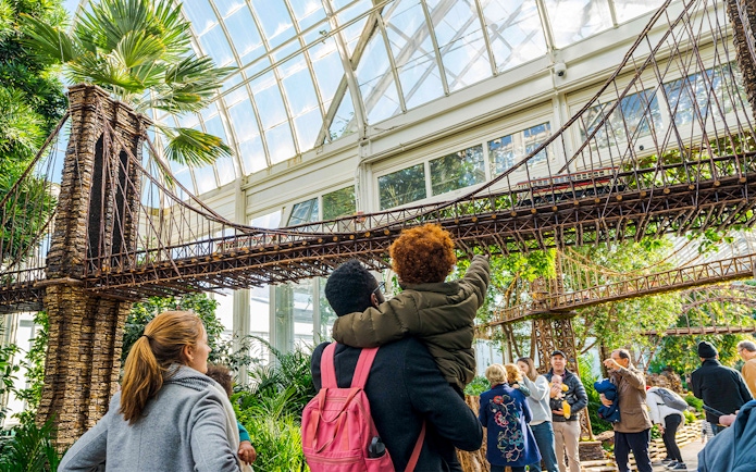 Visitors admire model bridges at New York Botanical Gardens, surrounded by greenery.