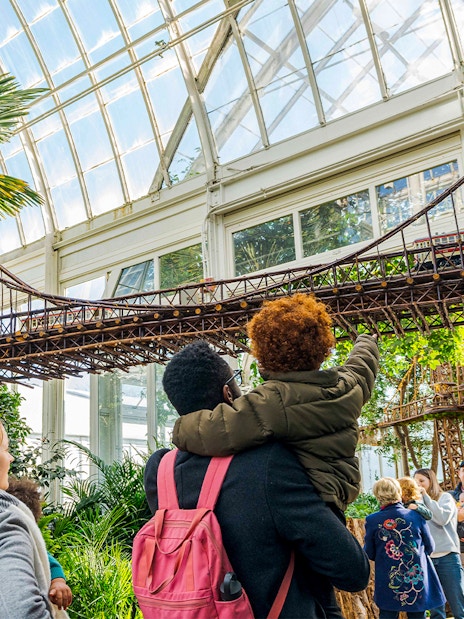 Visitors admire model bridges at New York Botanical Gardens, surrounded by greenery.