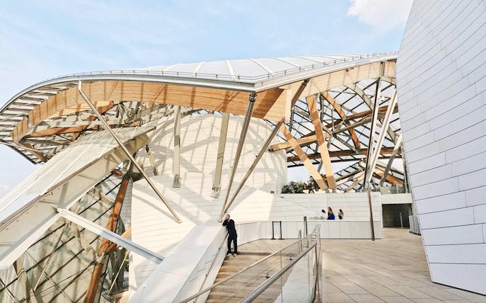 Person standing on stairs inside Louis Vuitton Foundation, Paris, with architectural details.