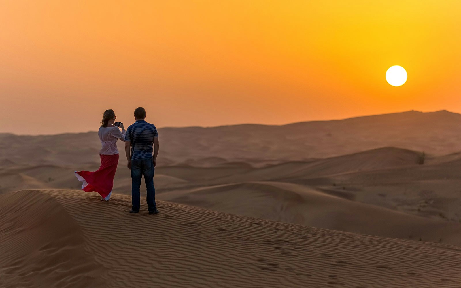Couple watching sunset over desert dunes during evening safari in Dubai.