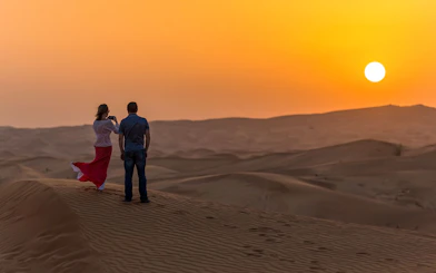 Couple watching sunset over desert dunes during evening safari in Dubai.