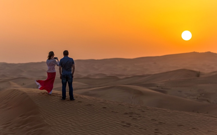 Couple watching sunset over desert dunes during evening safari in Dubai.