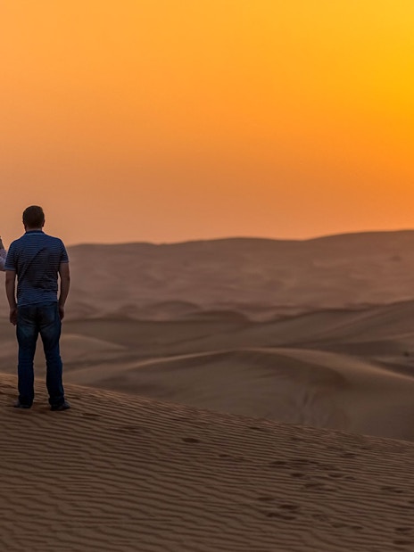 Couple watching sunset over desert dunes during evening safari in Dubai.