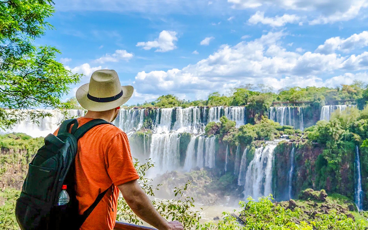 Traveler viewing Iguazu Falls in Argentina with lush greenery and cascading water.