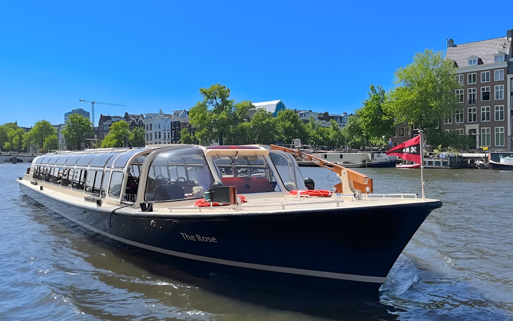Tour boat cruising Amsterdam canal with historic buildings in the background.