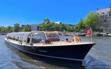 Tour boat cruising Amsterdam canal with historic buildings in the background.