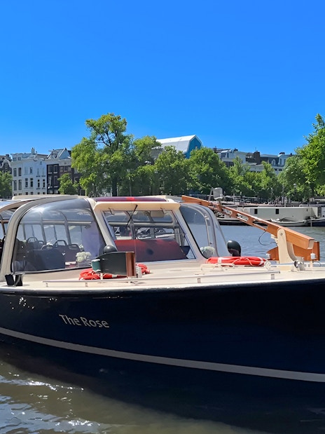 Tour boat cruising Amsterdam canal with historic buildings in the background.