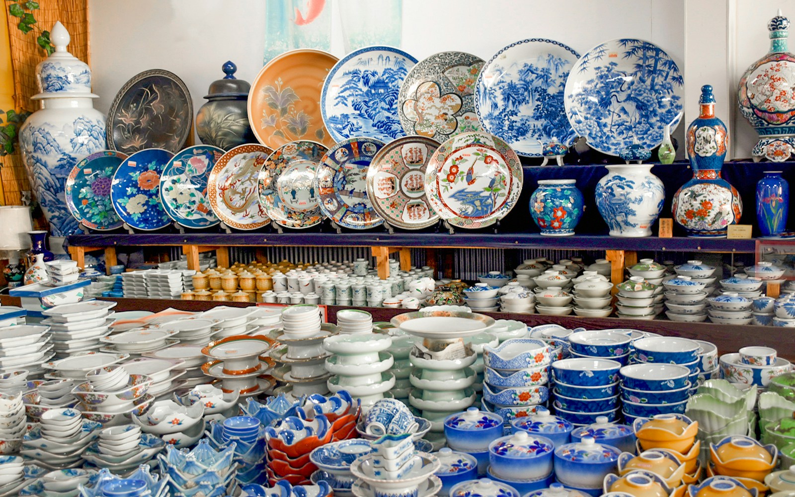 Japanese ceramics displayed at a market, featuring plates, bowls, and vases with intricate designs.