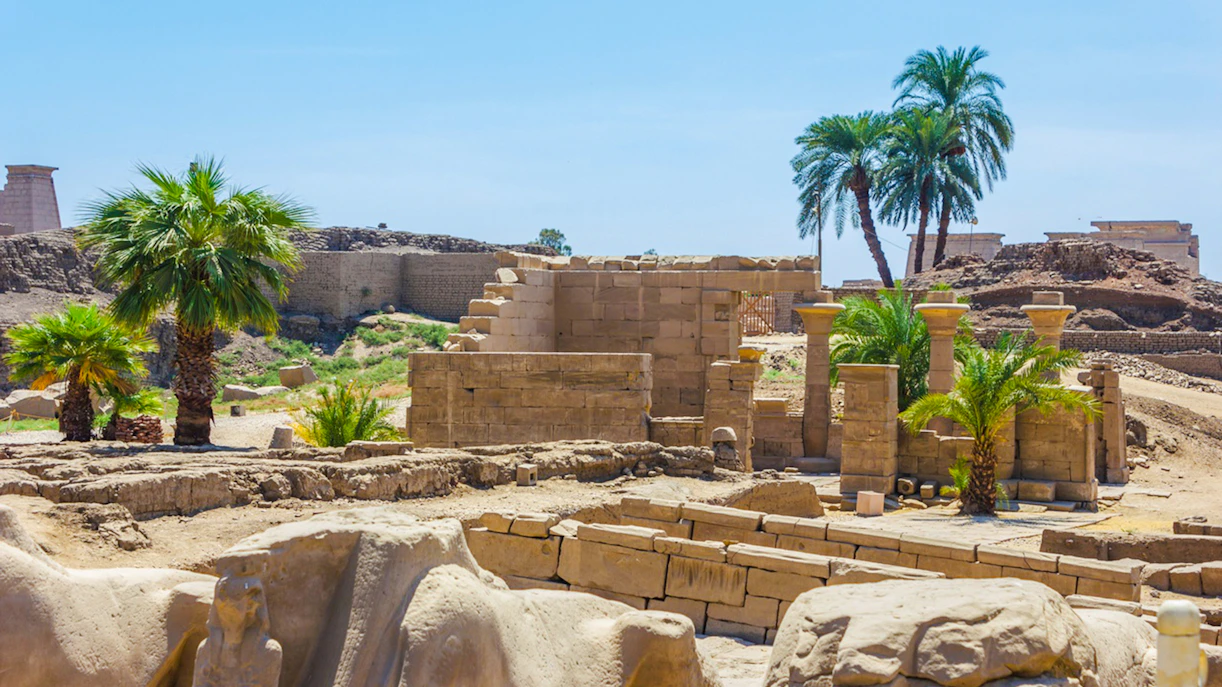 Ruins of Karnak Temple with ancient columns and palm trees in Luxor, Egypt.