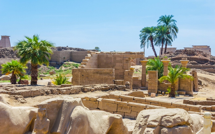 Ruins of Karnak Temple with ancient columns and palm trees in Luxor, Egypt.