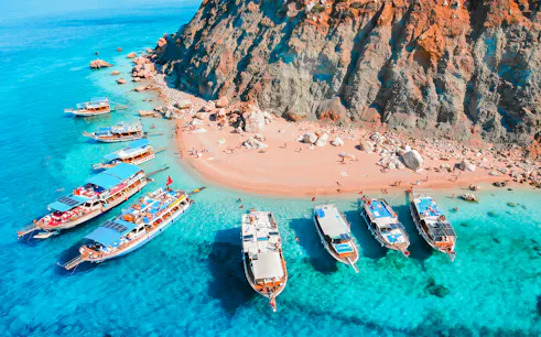 Boats anchored near Suluada Island's rocky shore and clear turquoise water.