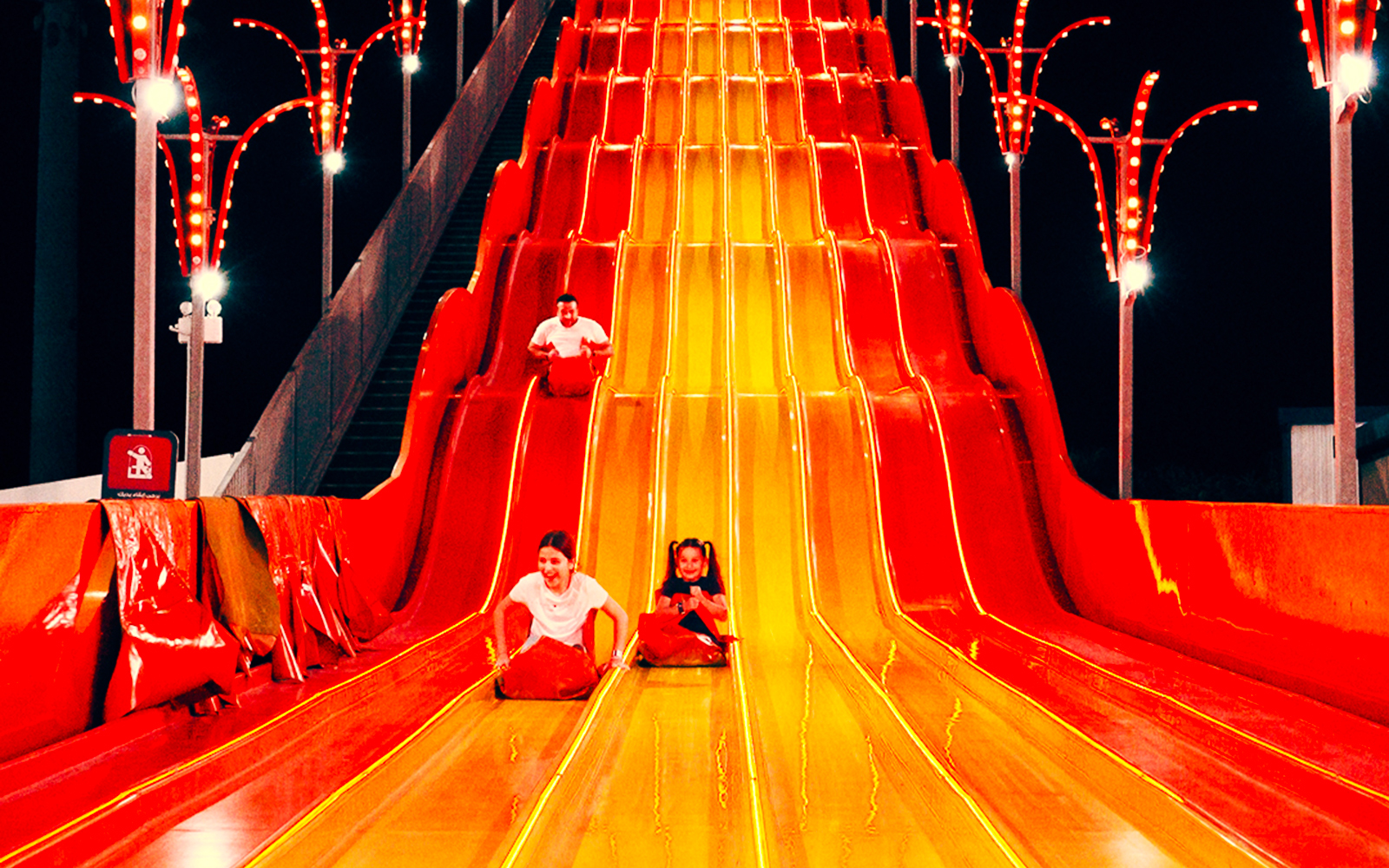 Children sliding down a colorful slide at Lusail Winter Wonderland.