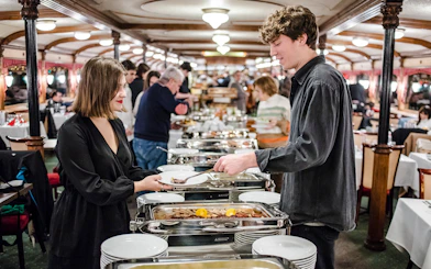 Couple enjoying buffet on Danube sightseeing dinner cruise at night.