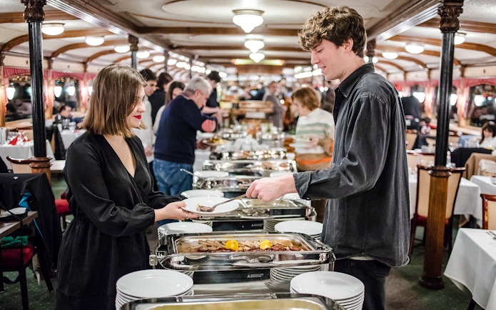 Couple enjoying buffet on Danube sightseeing dinner cruise at night.