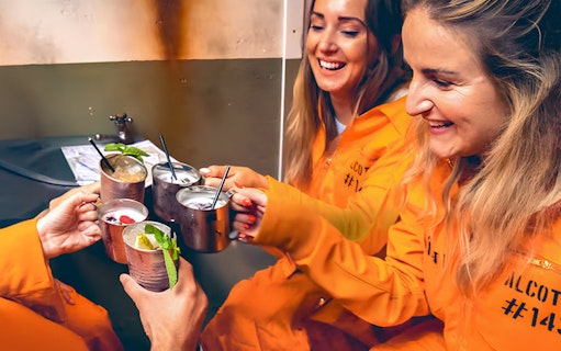 Guests in orange jumpsuits enjoying cocktails at Alcotraz prison-themed bar.