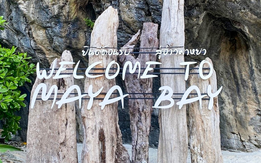 Welcome sign at Maya Bay Island with wooden posts and rocky background.