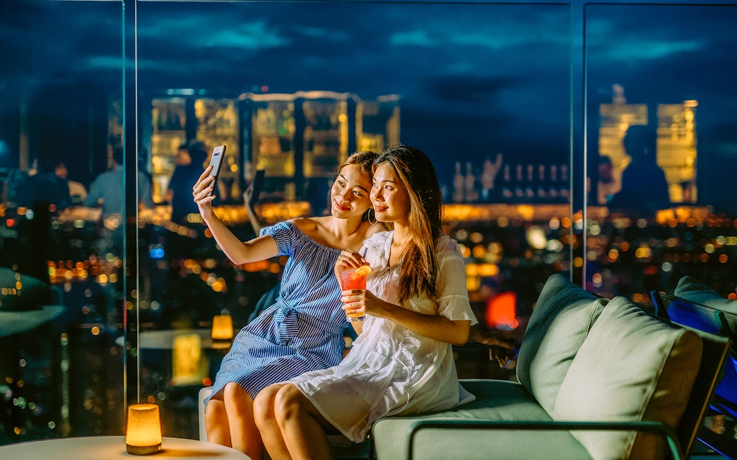 Friends taking a selfie on Mahanakhon SkyWalk, Bangkok, Thailand at night.