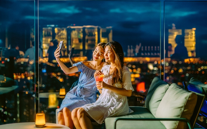 Friends taking a selfie on Mahanakhon SkyWalk, Bangkok, Thailand at night.