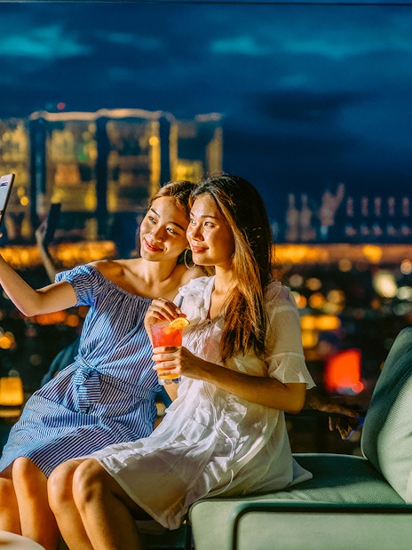 Friends taking a selfie on Mahanakhon SkyWalk, Bangkok, Thailand at night.