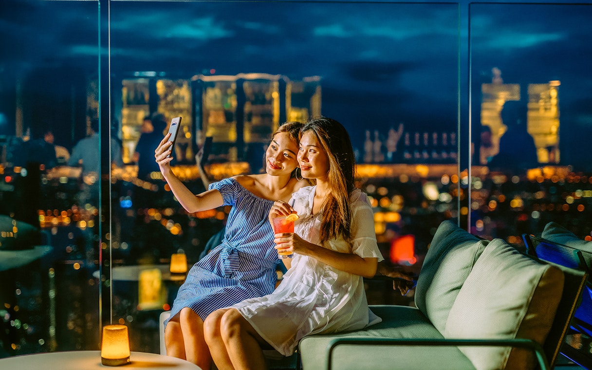 Friends taking a selfie on Mahanakhon SkyWalk, Bangkok, Thailand at night.