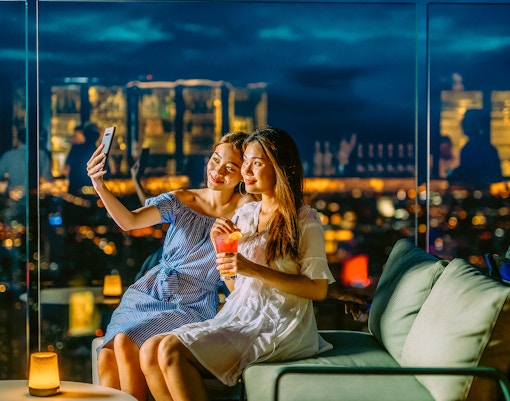 Friends taking a selfie on Mahanakhon SkyWalk, Bangkok, Thailand at night.