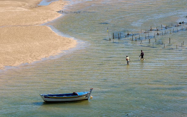Boat and people wading in shallow waters of Ria Formosa, Portugal.