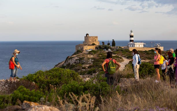 Group trekking near lighthouse on Colle of Sant'Elia, overlooking the sea.