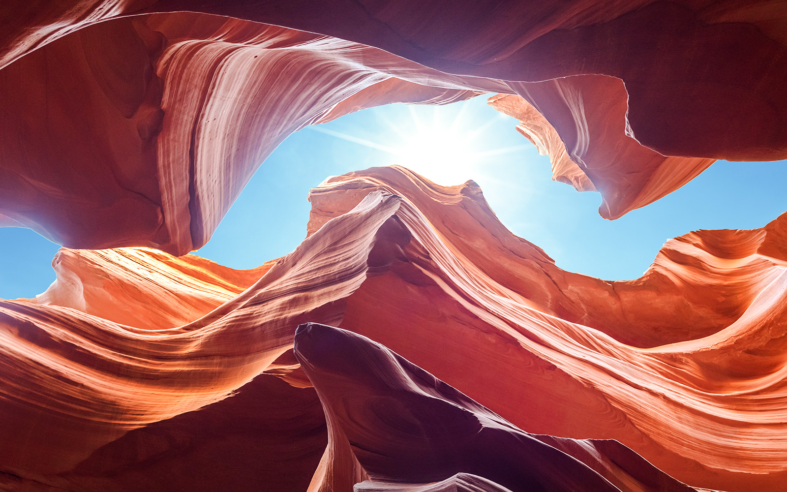 Antelope Canyon's swirling red rock formations under a bright blue sky, Arizona.
