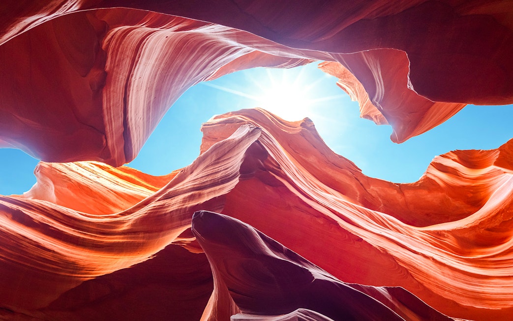 Antelope Canyon's swirling red rock formations under a bright blue sky, Arizona.