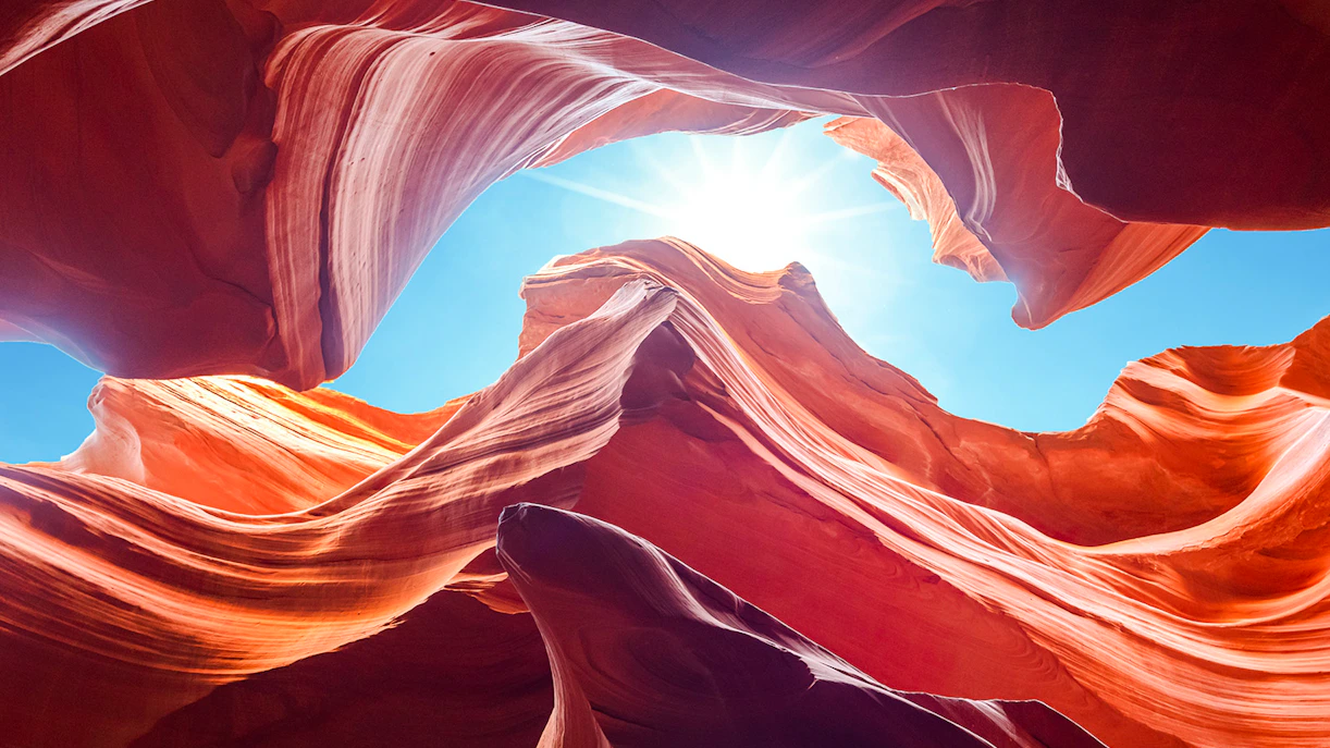 Antelope Canyon's swirling red rock formations under a bright blue sky, Arizona.