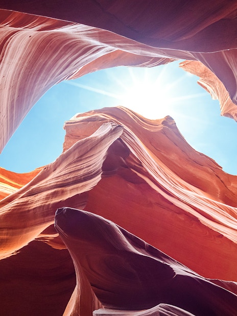 Antelope Canyon's swirling red rock formations under a bright blue sky, Arizona.
