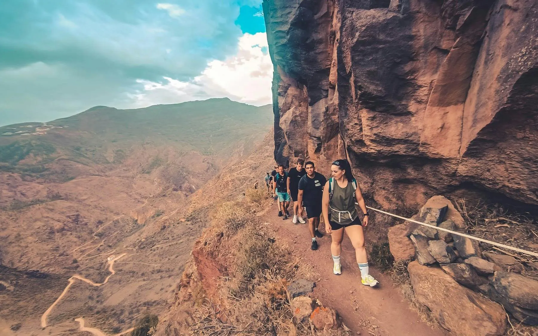Hikers on a narrow trail along a rocky cliff in Gran Canaria during a volcano sunset tour.