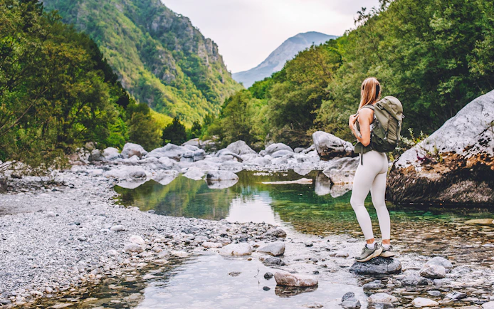 Woman hiking near Shala River in Tirana, surrounded by lush green mountains.
