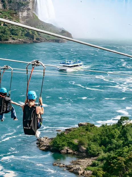 Ziplining over river towards waterfall with boat below, Niagara Falls.