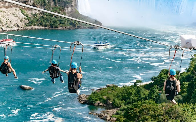 Ziplining over river towards waterfall with boat below, Niagara Falls.