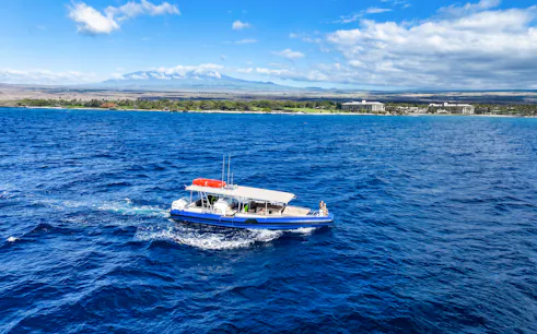Boat cruising along Big Island’s Kohala Coast with scenic shoreline in view.