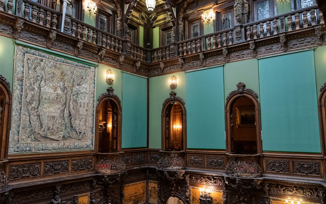 Hall of Honour in Peles Castle featuring ornate woodwork and a large tapestry.