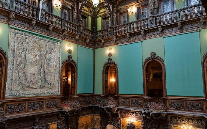 Hall of Honour in Peles Castle featuring ornate woodwork and a large tapestry.