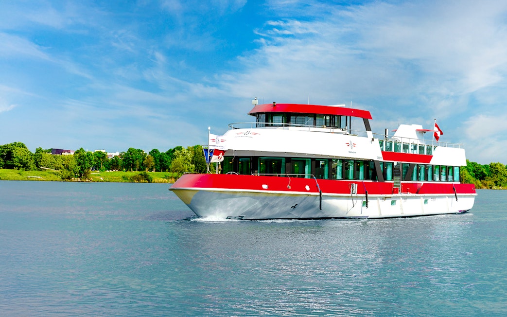 MS Vienna boat cruising on a river in Austria with lush green trees in the background.