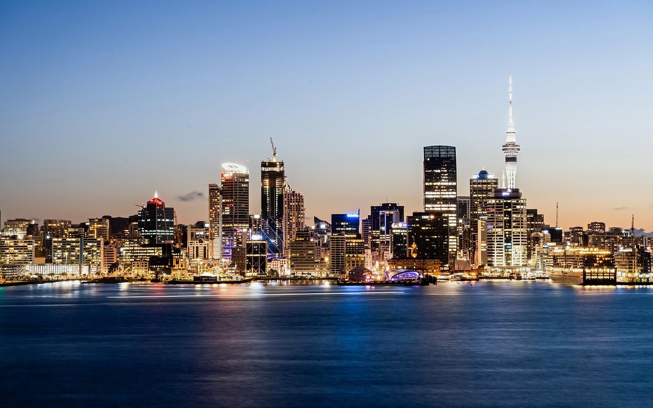 Auckland skyline at dusk viewed from the harbor, featuring illuminated buildings and Sky Tower.
