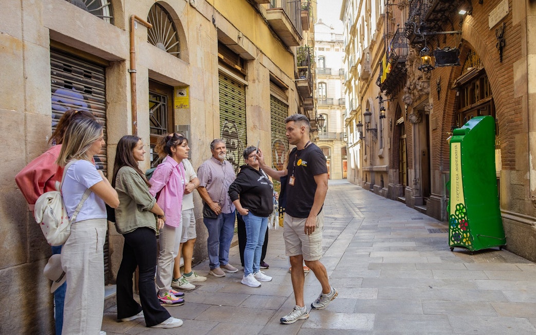 Tour group listening to a guide on a walking tour in a narrow street in Barcelona.
