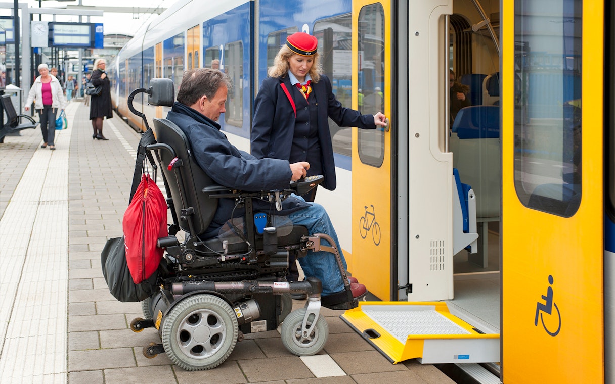 Wheelchair user boarding NS train at Schiphol Airport with assistance.