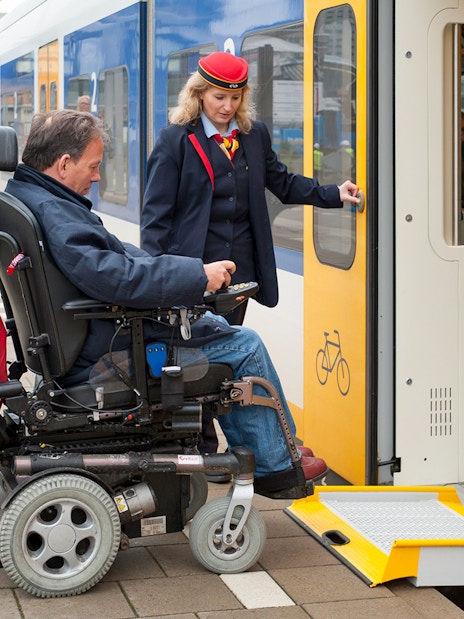Wheelchair user boarding NS train at Schiphol Airport with assistance.