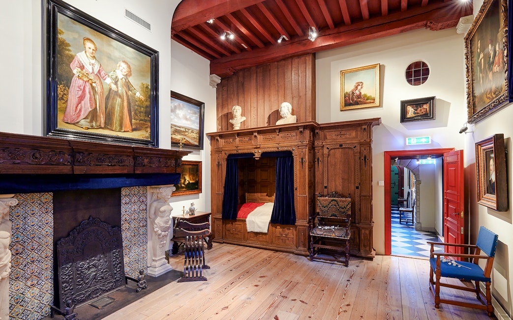 Interiors of the Rembrandt House Museum featuring a wooden bed, fireplace, and paintings.