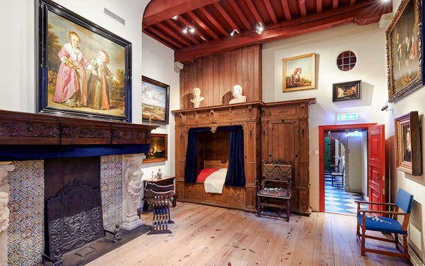 Interiors of the Rembrandt House Museum featuring a wooden bed, fireplace, and paintings.
